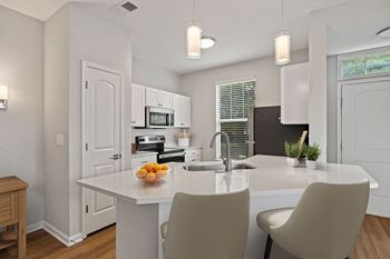 A kitchen with white cabinets and a white island with a bowl of fruit on it
